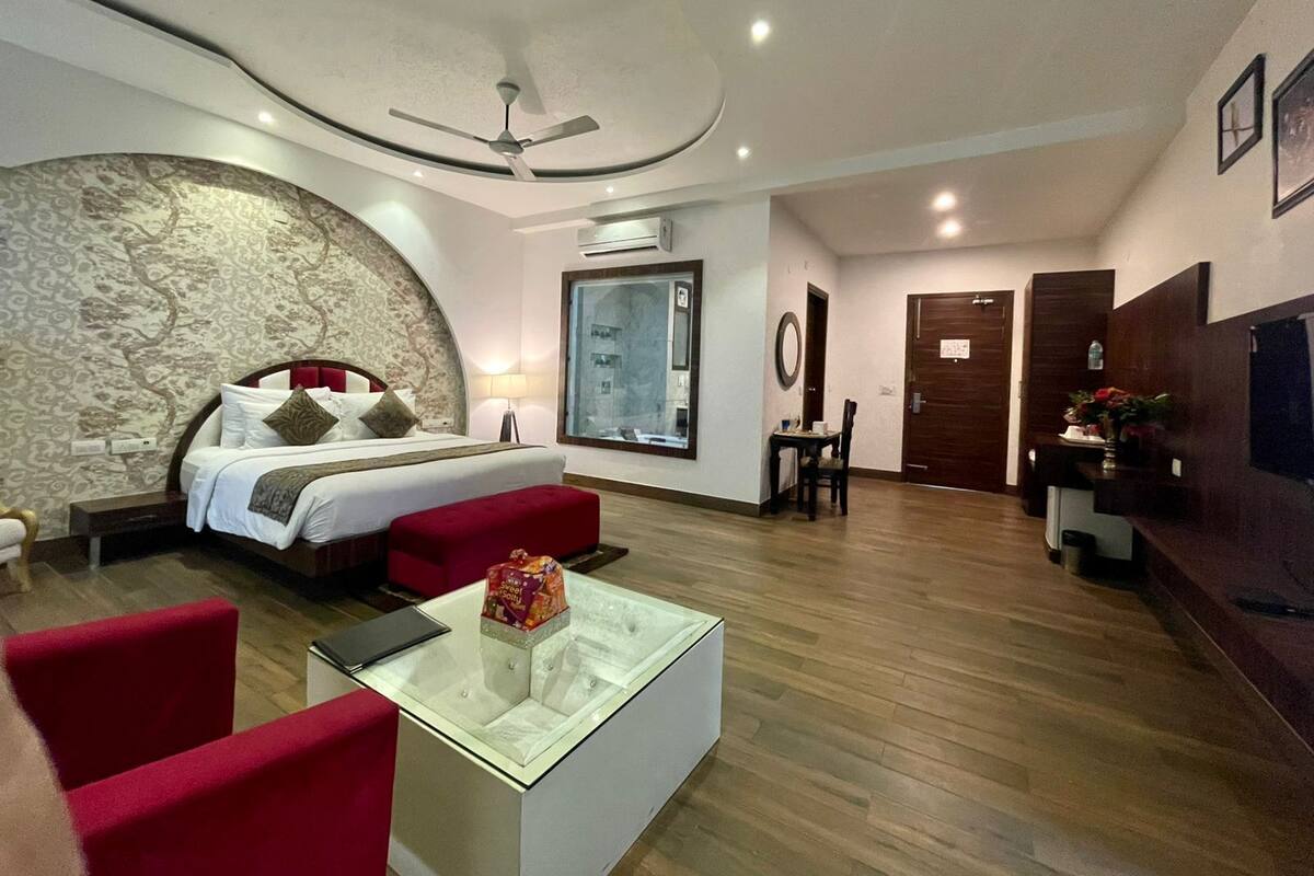 A modern hotel room with a curved stone wall, a bed with red and white bedding, a glass coffee table, and a red armchair.