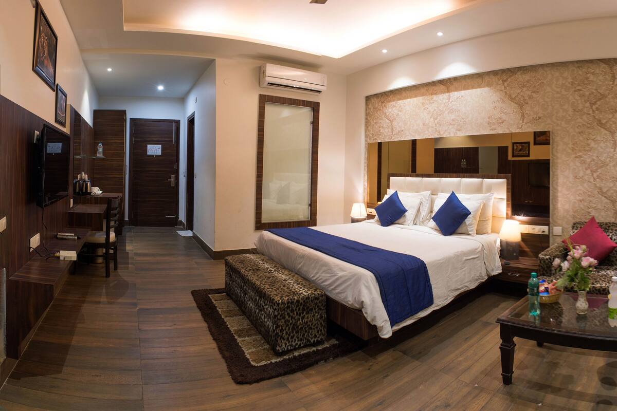 A hotel room with a bed, bedside table, lamp, and a seating area with a sofa and armchair.