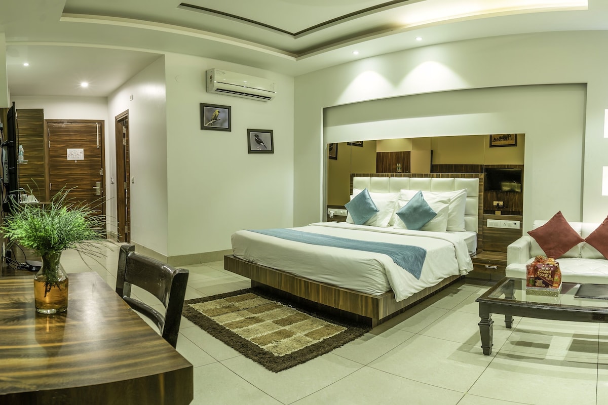 A hotel room with a bed, a desk, a chair, a coffee table, and a potted plant.