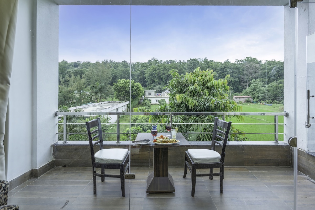 A balcony with a table and chairs, overlooking a lush green landscape with trees and buildings.
