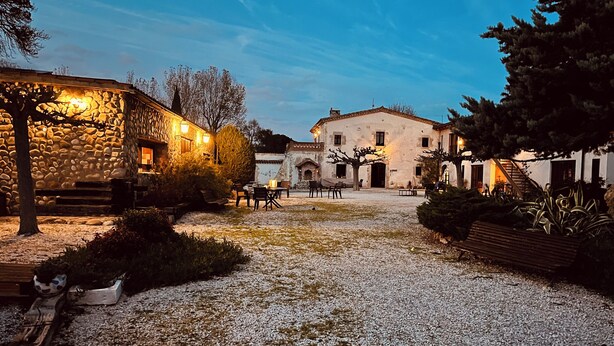 A courtyard with stone walls, outdoor seating, and a building with a tiled roof. - B&B El Ranxo (Caldes de Malavella)