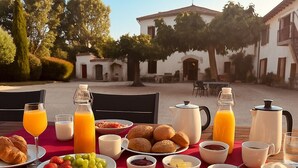 A breakfast table set outdoors with various food items, drinks, and a view of a courtyard with buildings. - B&B El Ranxo (Caldes de Malavella)