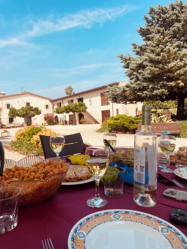 A table set for a meal with a bottle of wine, glasses, and plates, overlooking a building with a garden.