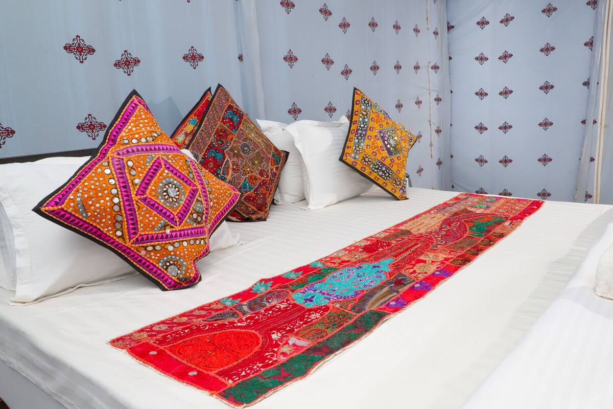 Un lit agrémenté de coussins aux couleurs vives et d’un chemin de table rouge et vert à motifs.