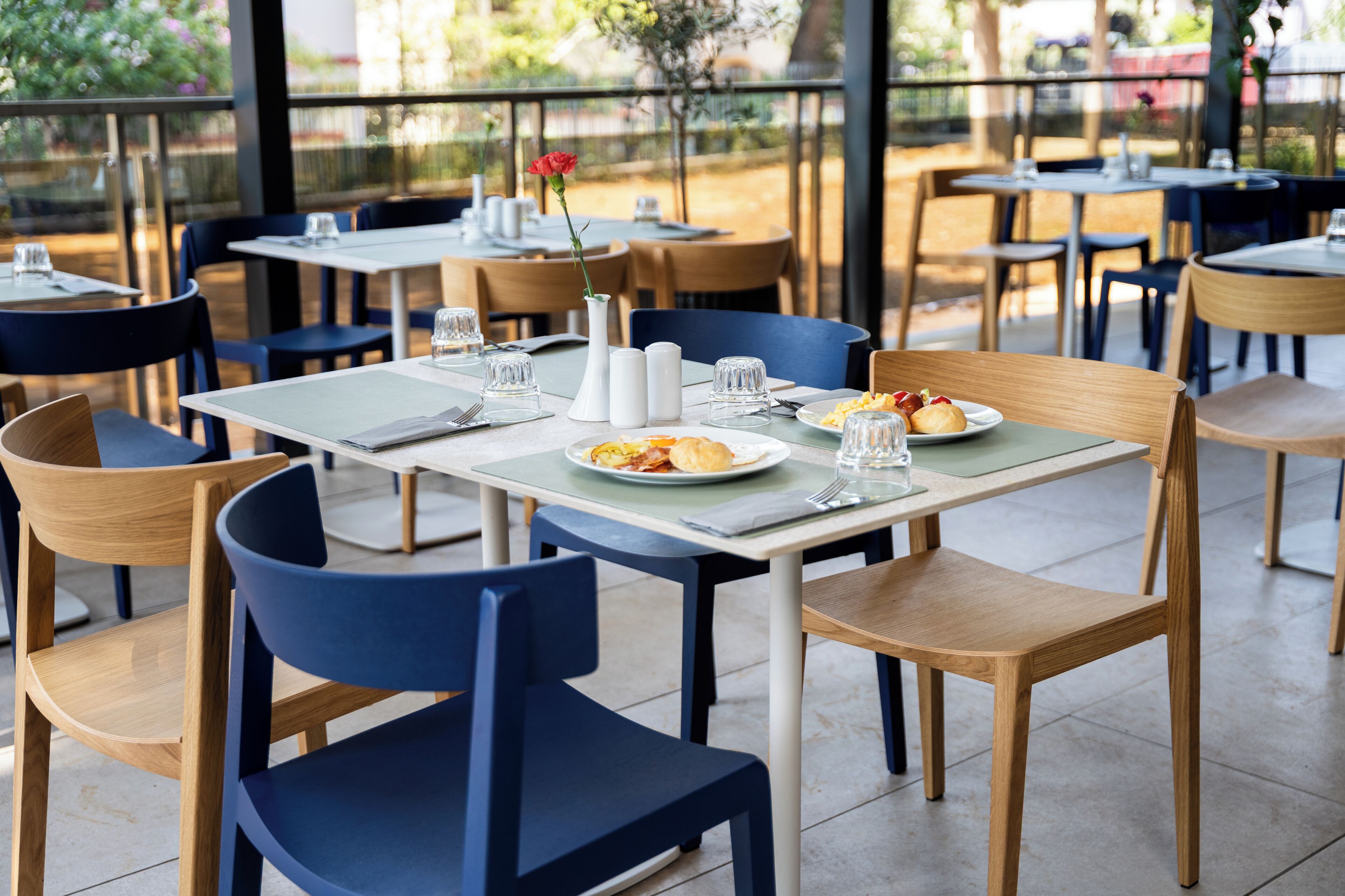 A restaurant with tables and chairs, plates of food, and a vase with a flower.