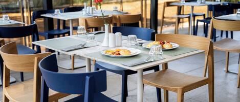 A restaurant with tables and chairs, plates of food, and a vase with a flower.