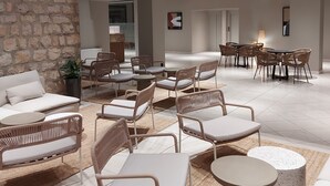 A modern lounge area with wicker furniture, a stone wall, and a view of the interior space. - Family Hotel Adria (Biograd na Moru)