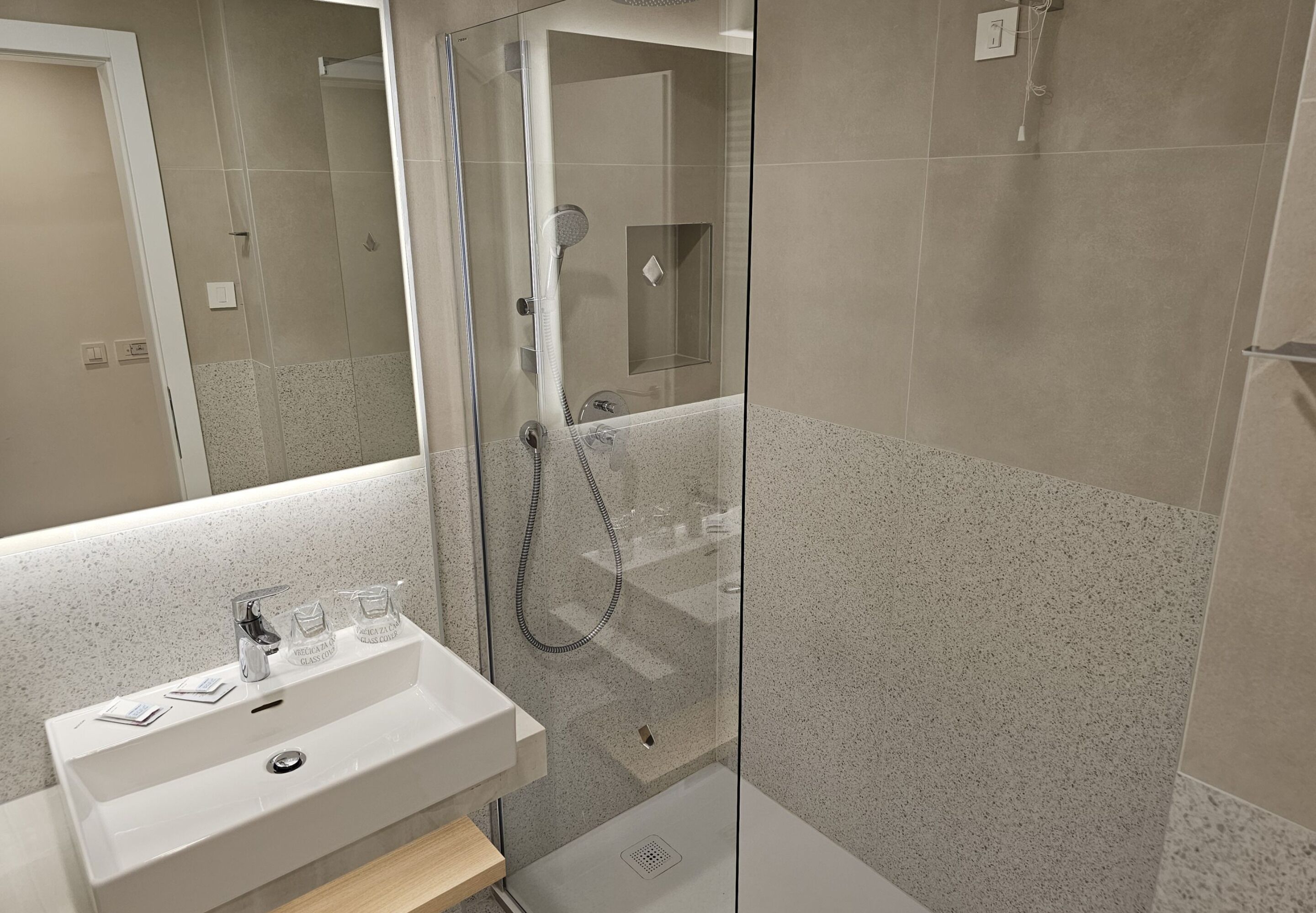 A modern bathroom with a glass-enclosed shower, a white sink with a mirror, and a speckled tile backsplash.