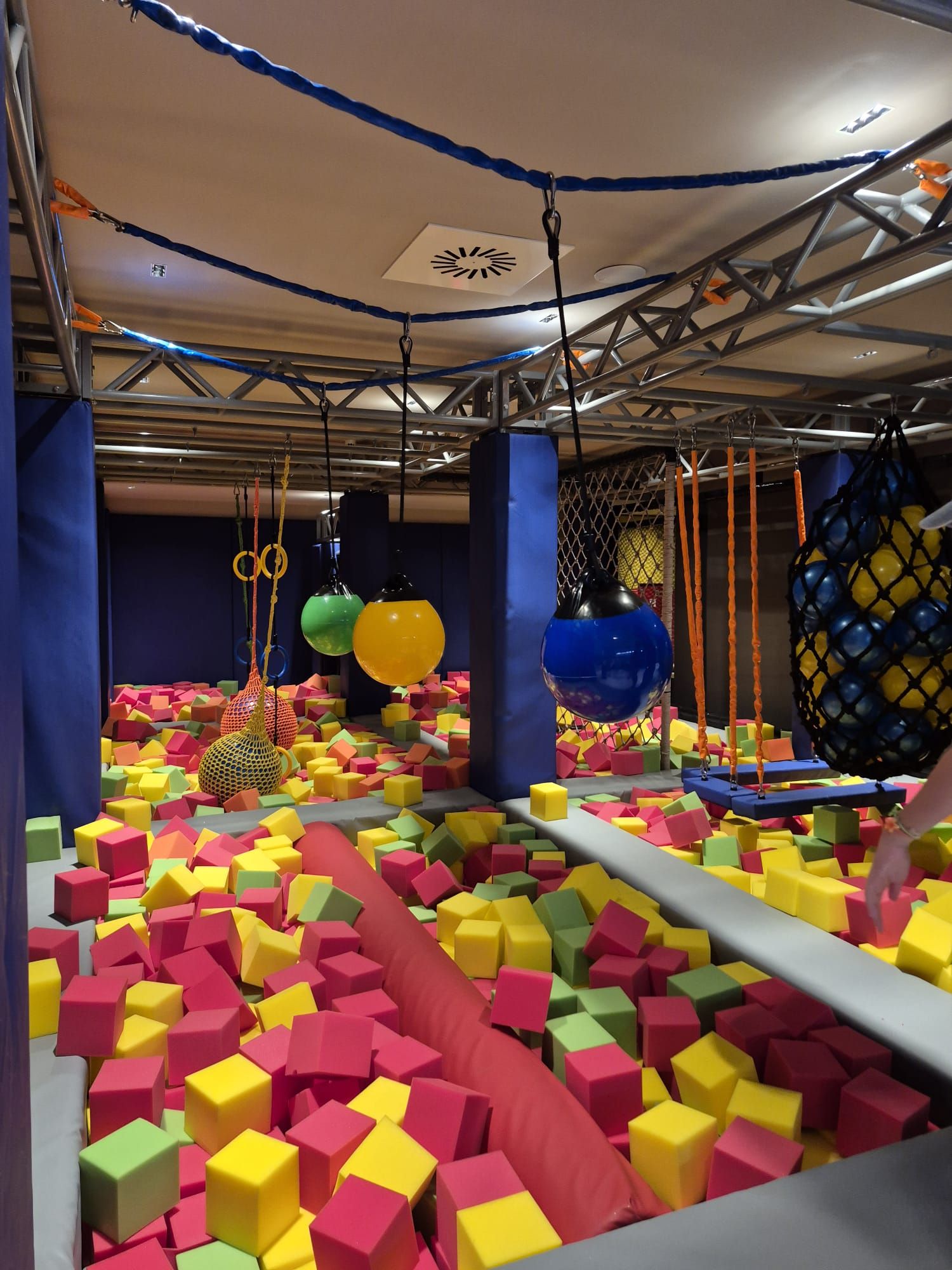 An indoor play area with foam blocks, hanging rings, and netted climbing structures.