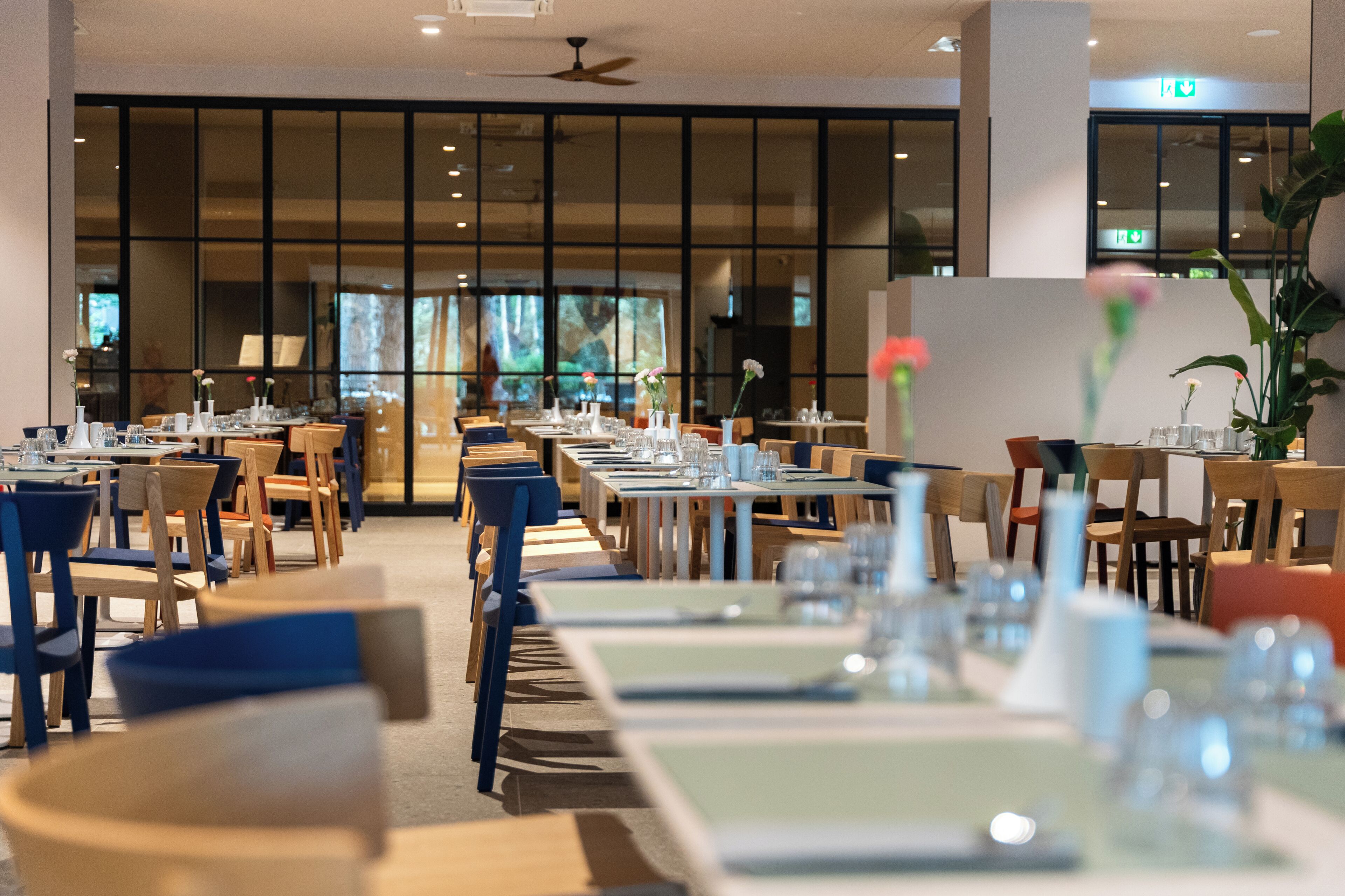 A restaurant with multiple tables and chairs, large windows, and a ceiling fan.