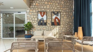 Una sala de estar moderna con pared de piedra, un sofá, sillones de mimbre y un ventanal con cortinas.