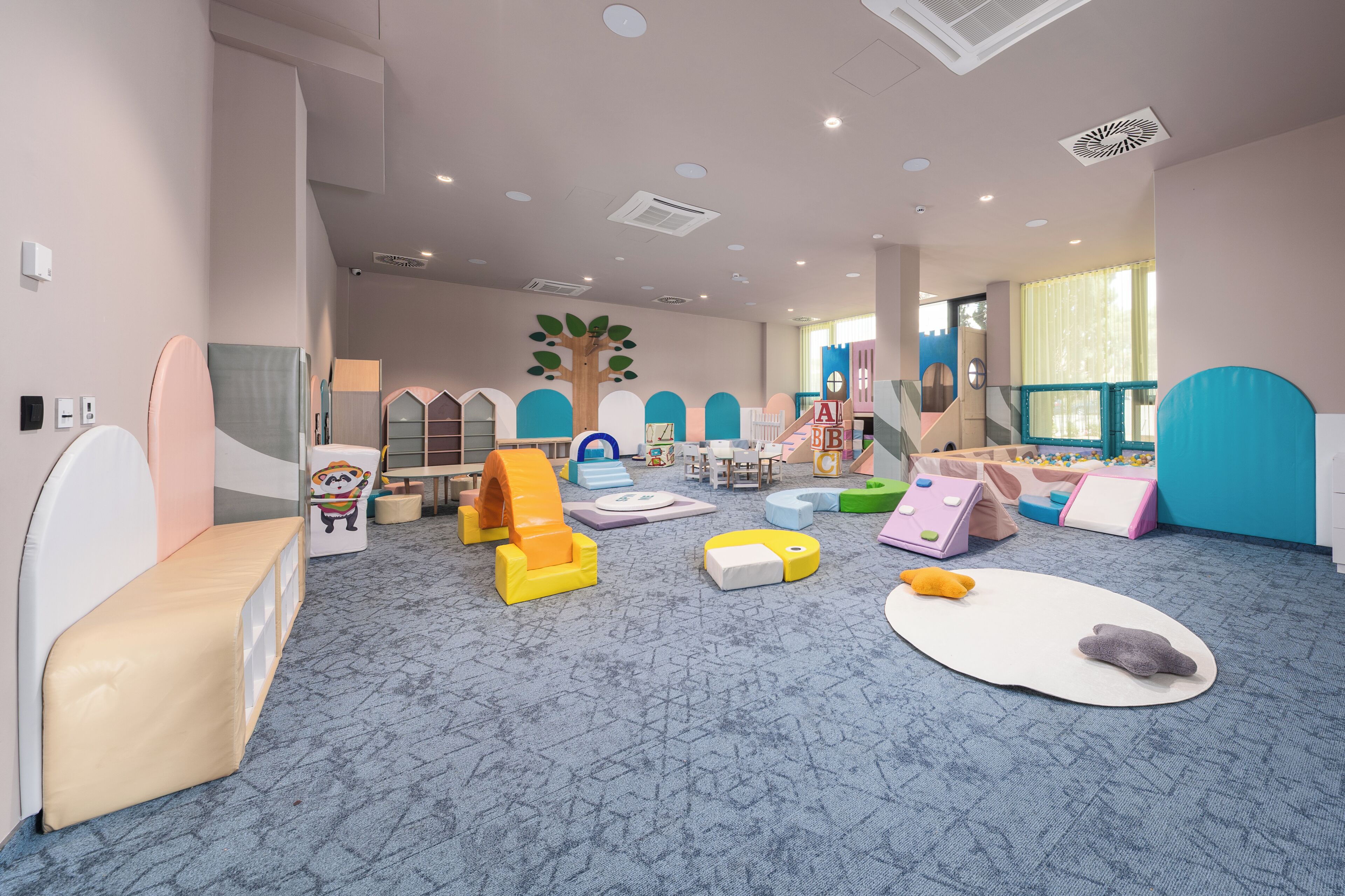 A children's playroom with soft play mats, foam blocks, and a large tree decoration.