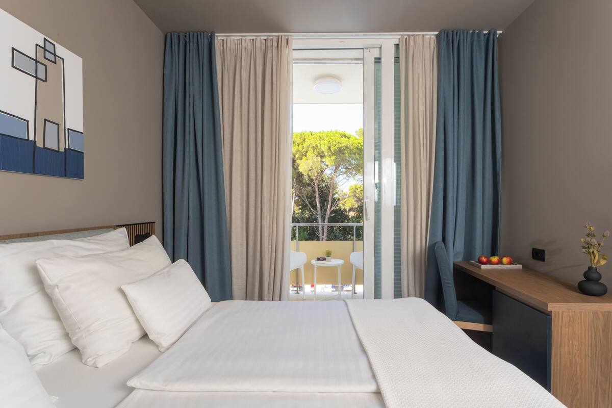 A hotel room with a bed, a desk, and a balcony with a table and chairs.