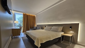 A modern hotel room with a large bed, a bedside table, a desk with a chair, and a view of the outdoors. - Family Hotel Adria (Biograd na Moru)