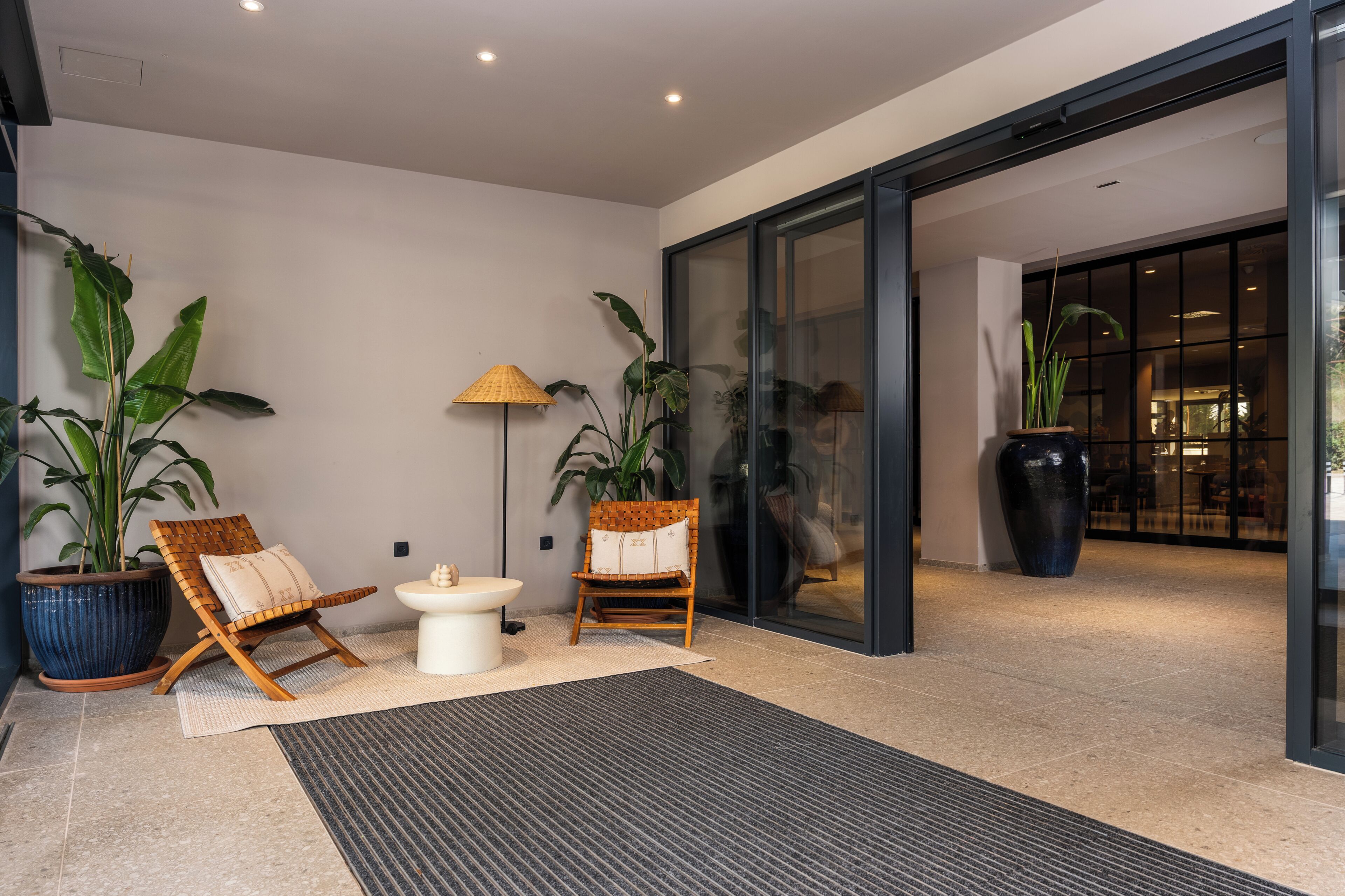 A modern interior with two wicker chairs, a small table, and large potted plants.