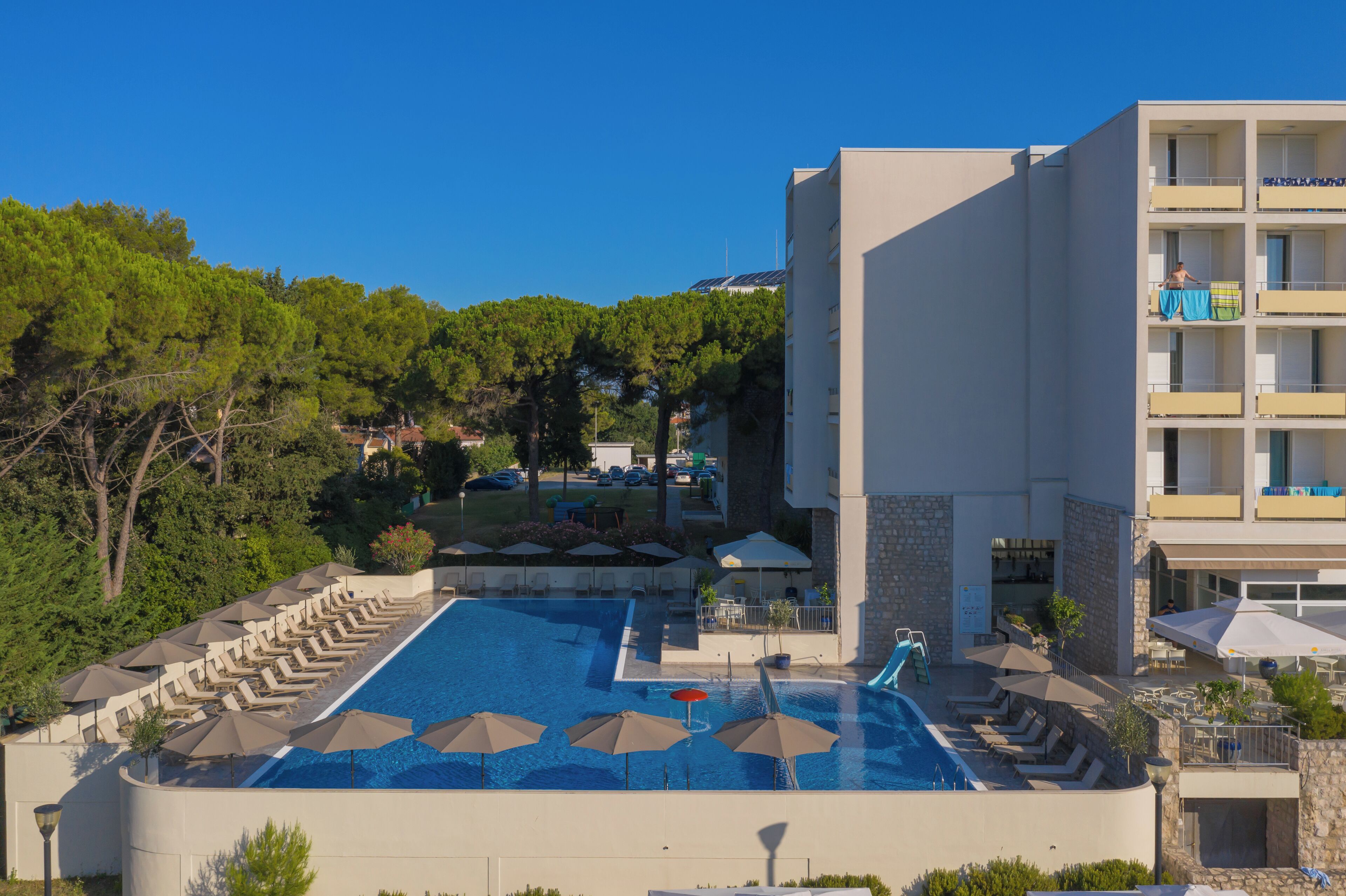 A hotel with a swimming pool, outdoor seating, and a view of the surrounding area.