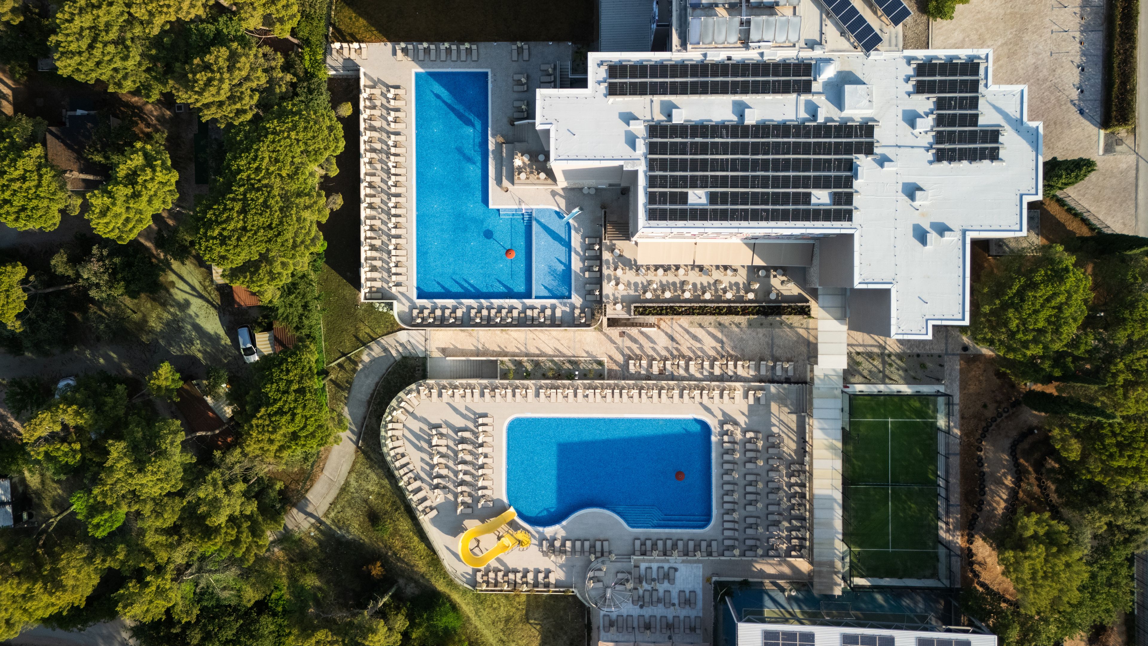 Vista aérea de una propiedad con dos piscinas, una cancha de tenis y paneles solares.