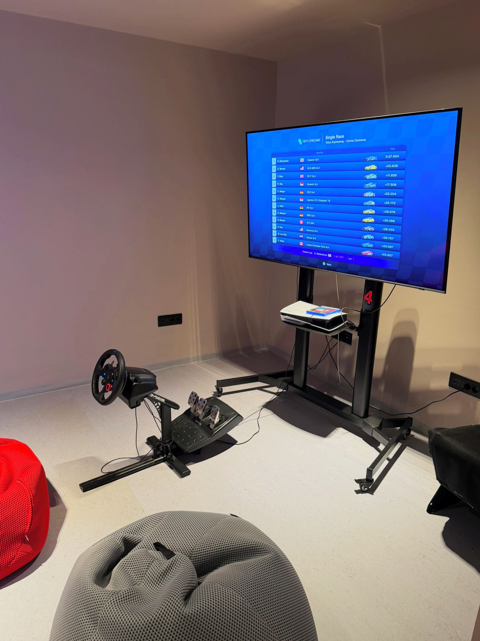 A gaming setup with a monitor displaying a racing game, a steering wheel, pedals, and a VR headset.