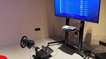 A gaming setup with a monitor displaying a racing game, a steering wheel, pedals, and a VR headset.