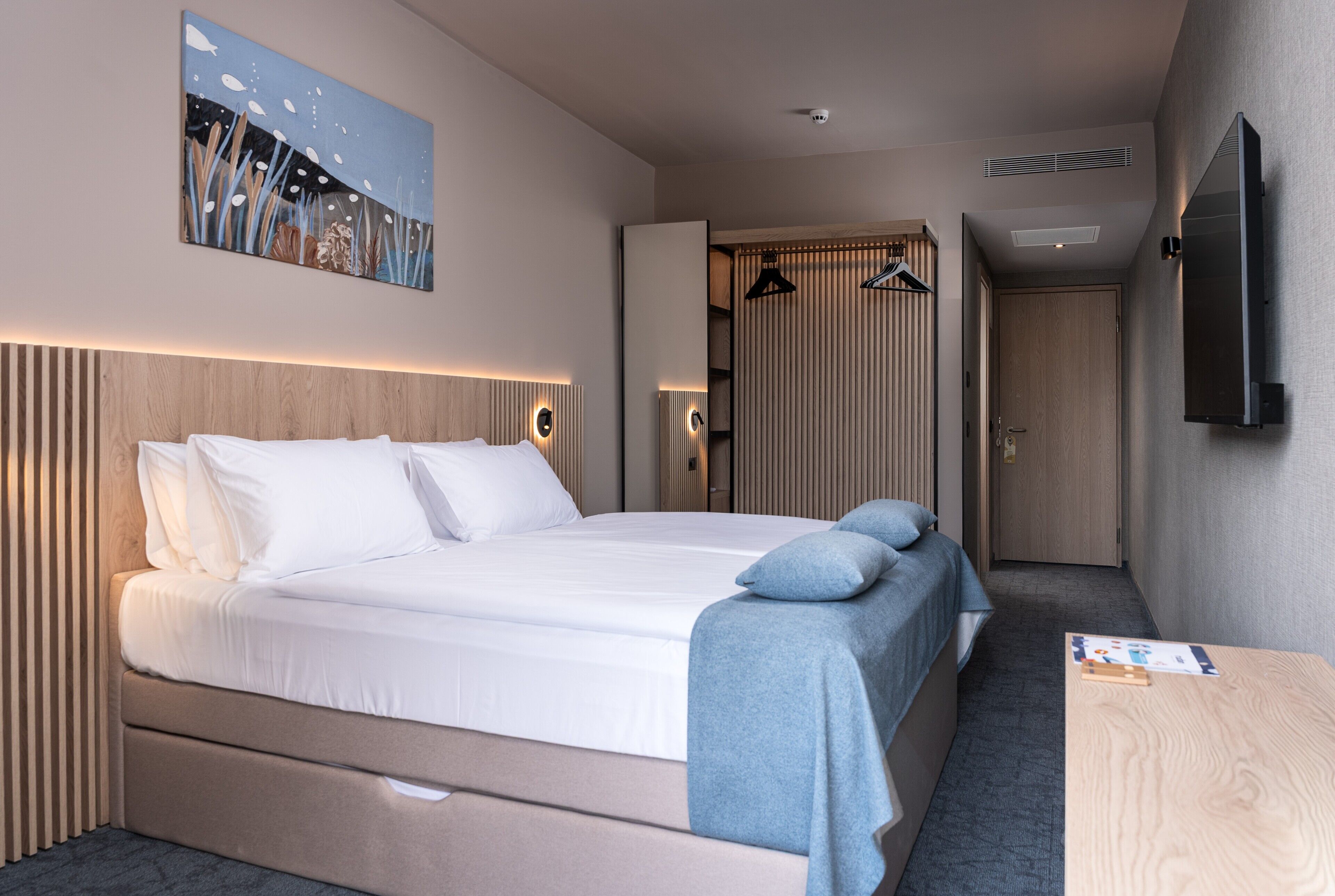 A hotel room with a bed, bedside tables, a flat-screen TV, a painting on the wall, and a wardrobe.