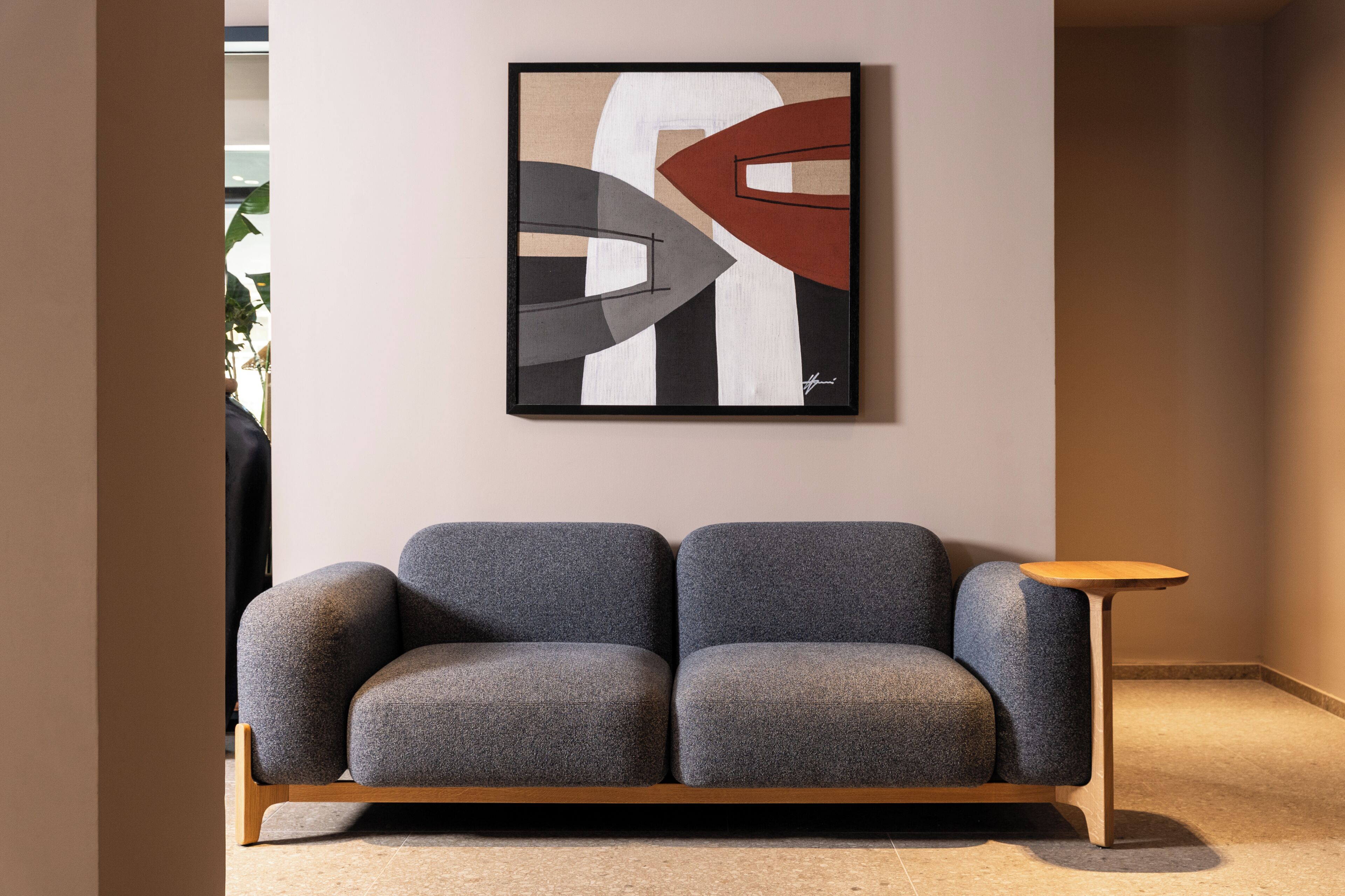 A modern living room with a grey sofa, a wooden side table, and a framed abstract painting on the wall.