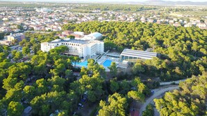 An aerial view of a resort with a large building, a swimming pool, and dense surrounding greenery. - Family Hotel Adria (Biograd na Moru)