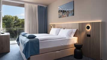 Een moderne slaapkamer met een groot bed, een bijzettafeltje, een klein krukje en uitzicht op het omliggende landschap.