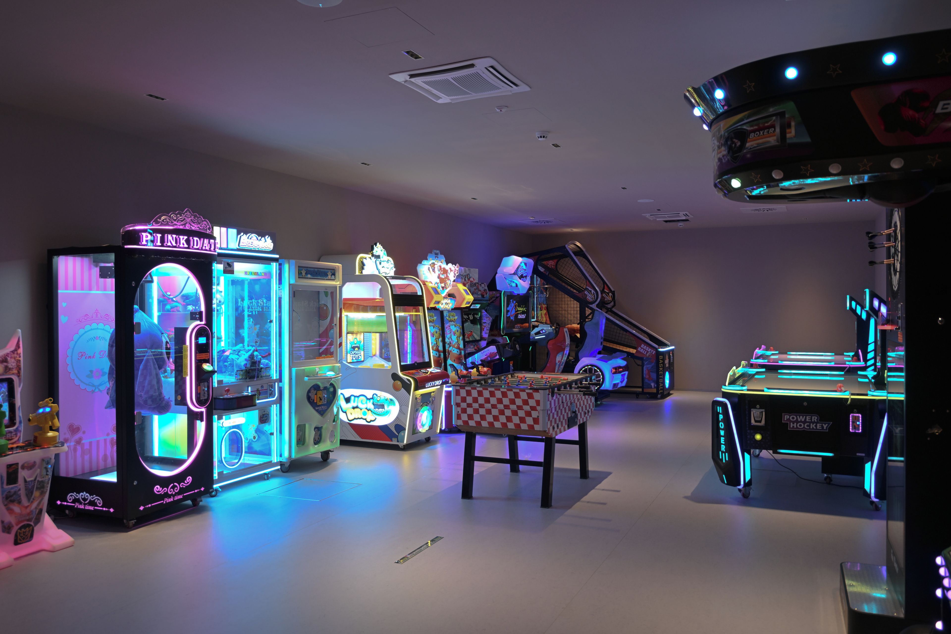 Variedad de juegos de arcade y mesas de futbolín en un espacio interior con poca luz.