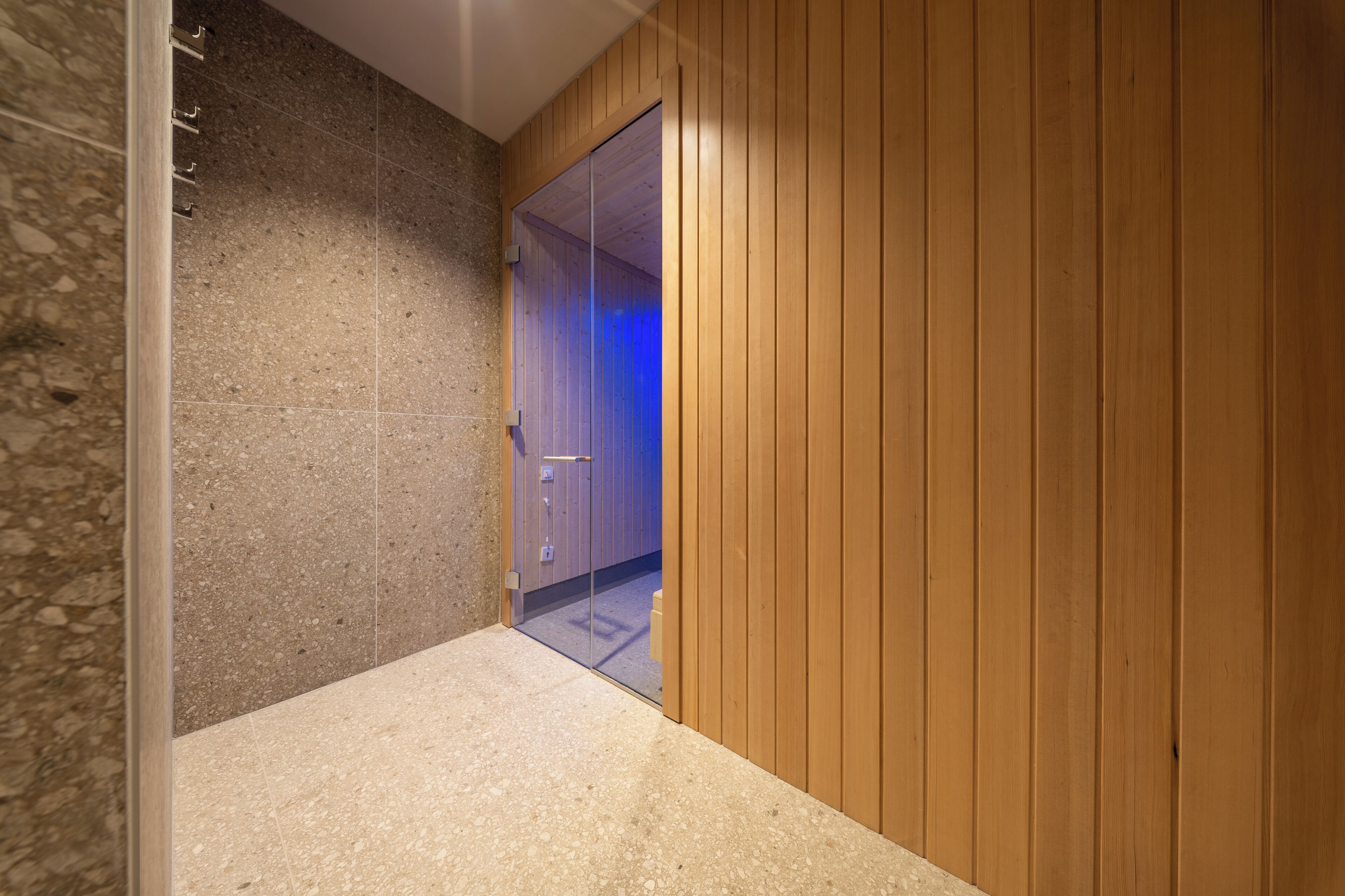 Un pasillo con una pared de piedra en un lado y paneles de madera en el otro, que conduce a una habitación con una puerta.