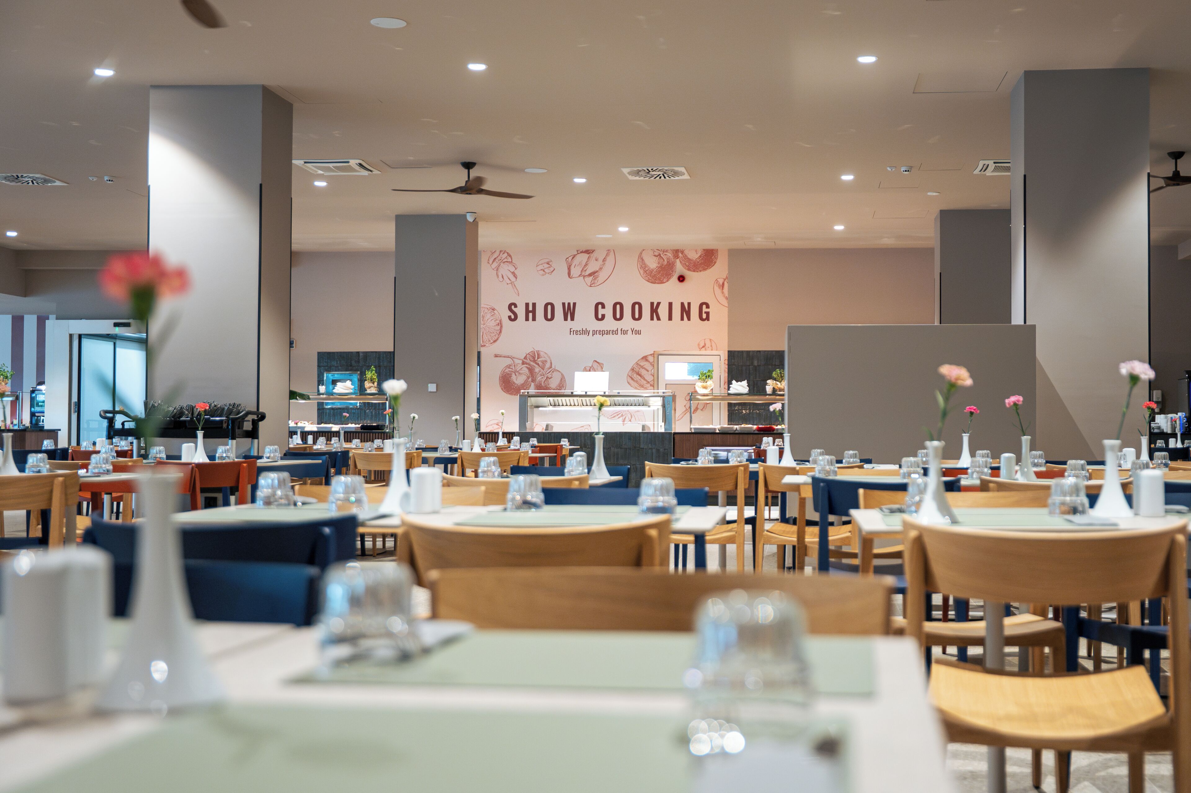 Interior de restaurante con varias mesas, sillas y una pared con el letrero 'SHOW COOKING'.