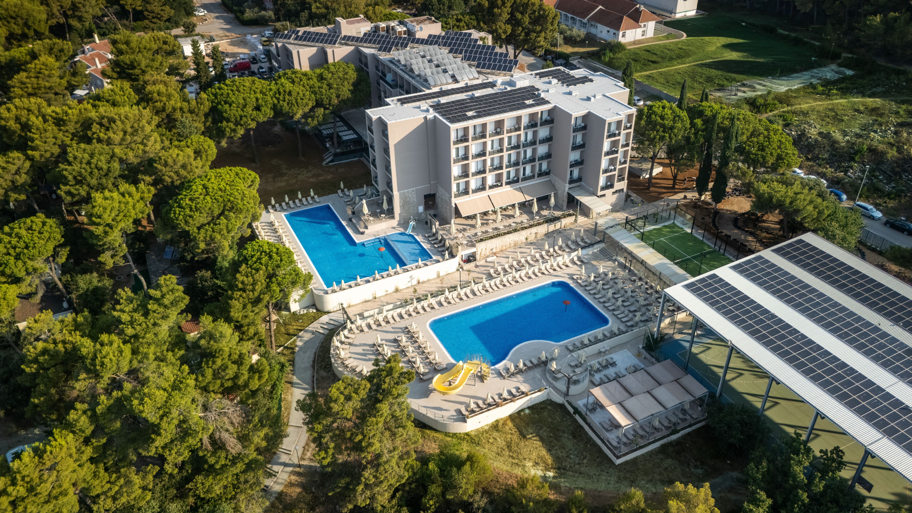 Vue aérienne d’un hôtel doté de plusieurs piscines, d’un espace de jeux pour enfants et de panneaux solaires.