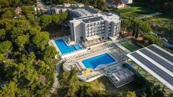 Vue aérienne d’un hôtel doté de plusieurs piscines, d’un espace de jeux pour enfants et de panneaux solaires.