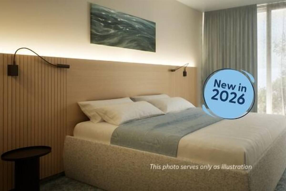 A hotel room with a bed, a bedside table, a wall-mounted TV, and a window with curtains.