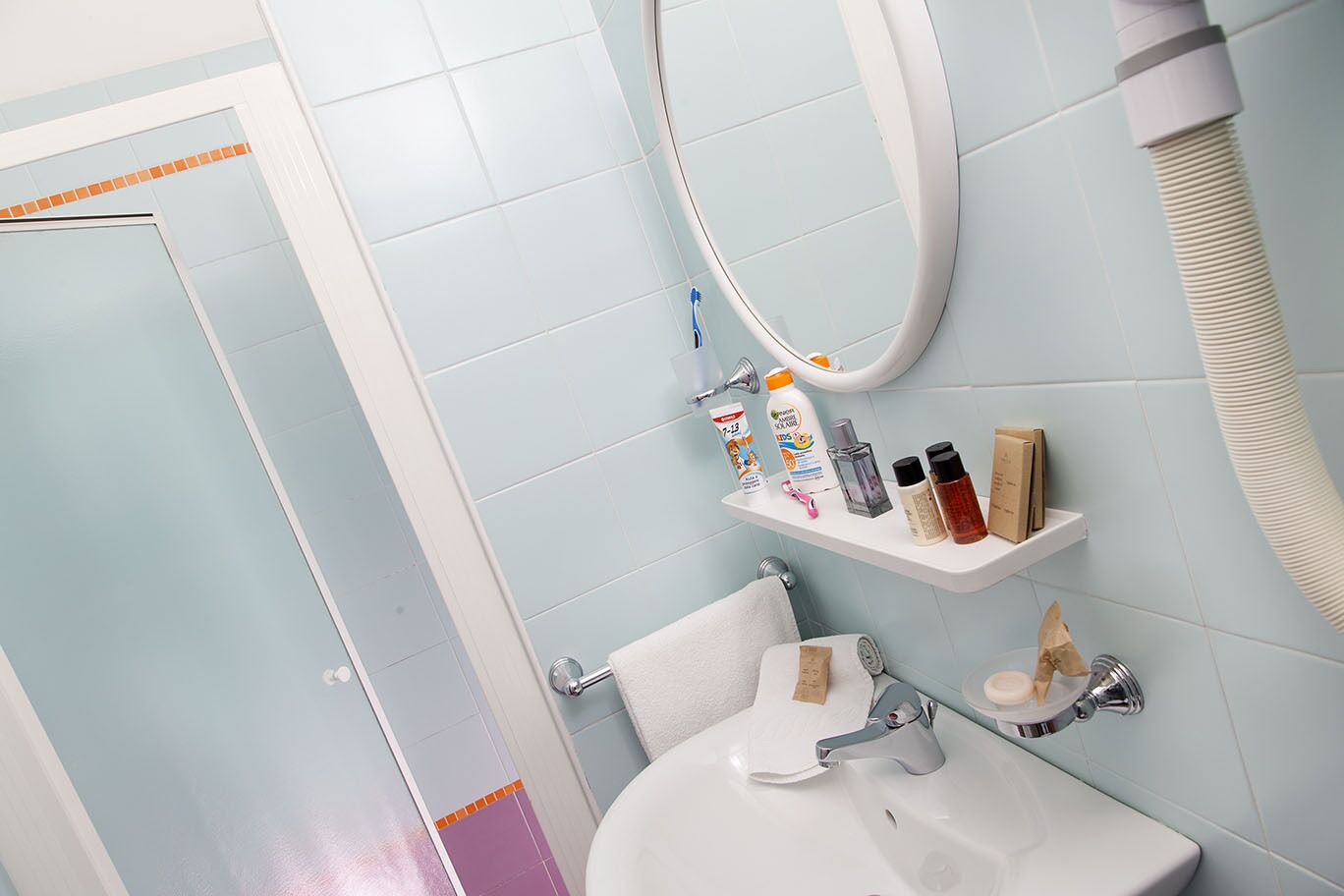 A bathroom with a white sink, a mirror, and a shelf with toiletries.