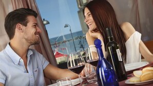 Una pareja cenando en una mesa con copas de vino, una botella y pan.