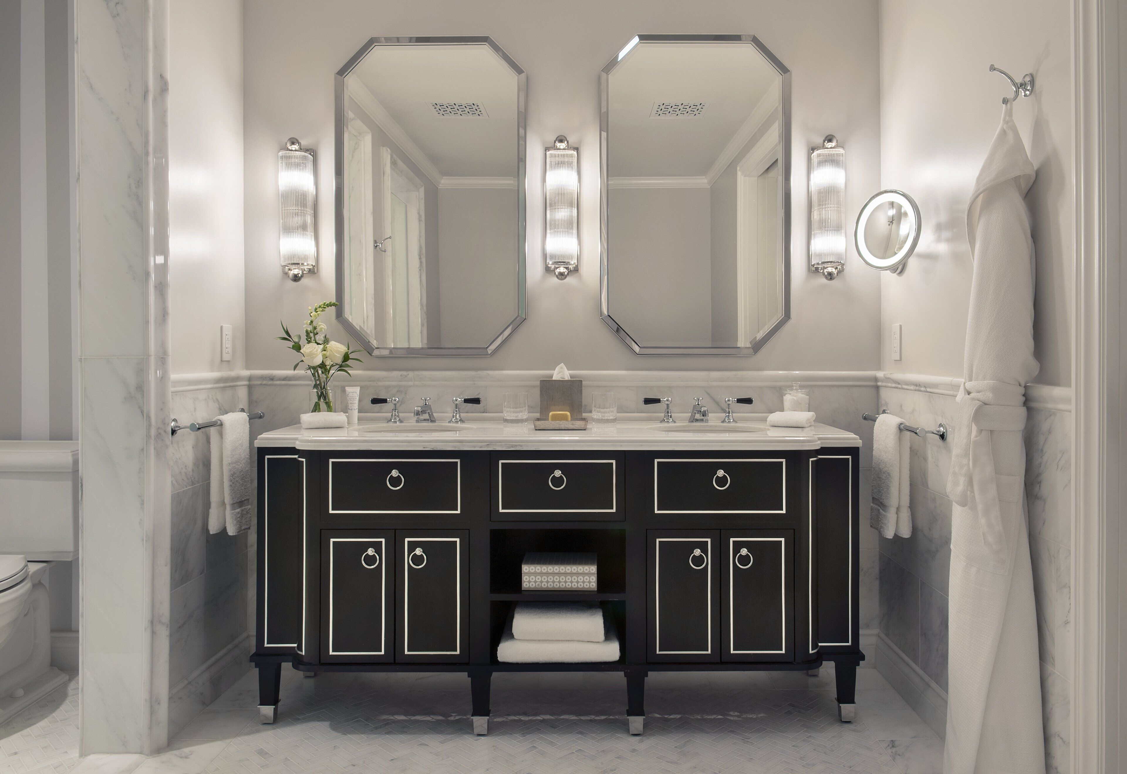 A bathroom with a black vanity, two large mirrors, and a towel rack.