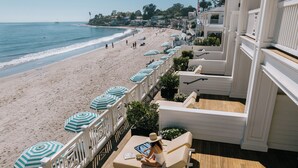 Een terras met buitenmeubels en parasols met uitzicht op een strand.