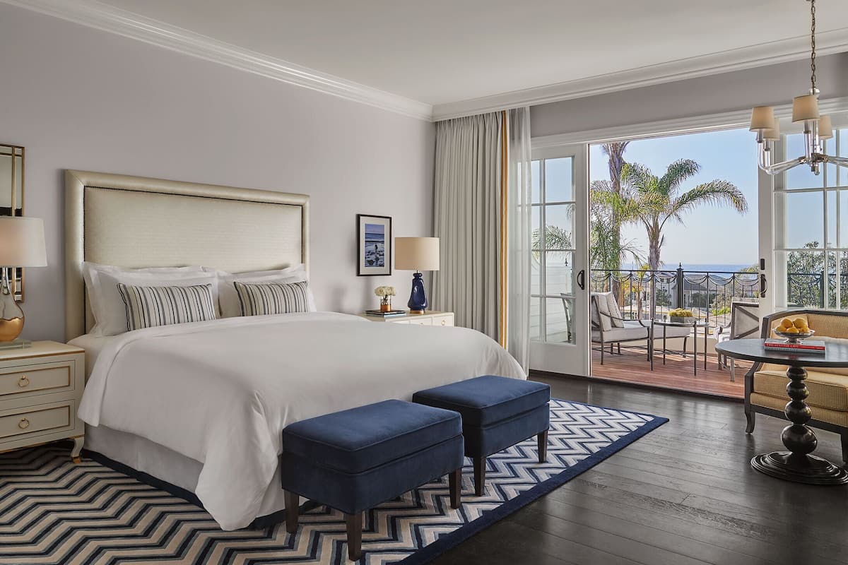 Hotelkamer met een groot bed, een bureau met stoel en een balkon met uitzicht op palmbomen en de oceaan.