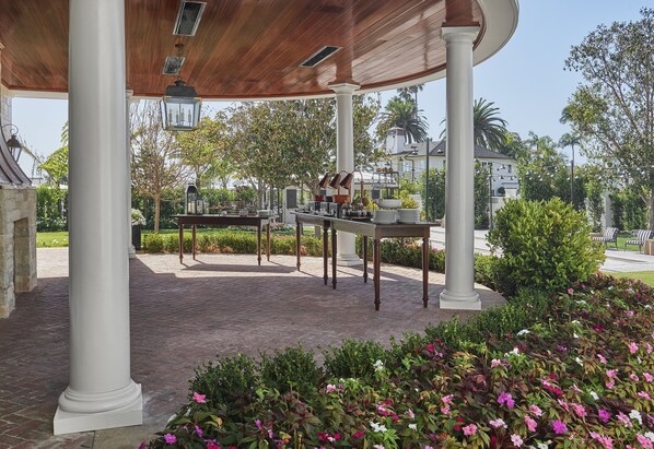 A covered outdoor area with a brick floor, white columns, and a table with chairs.