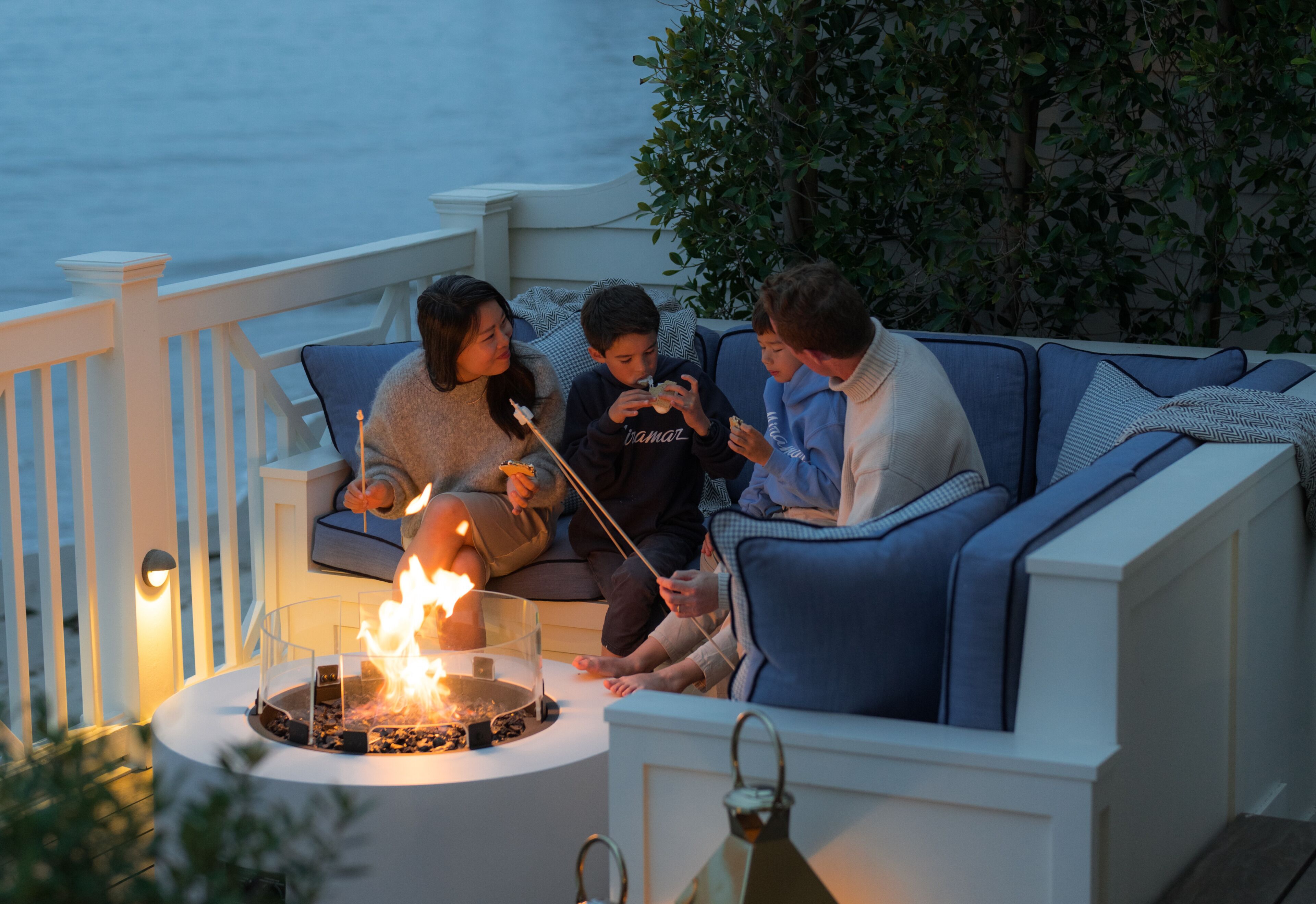 A family sitting on a blue sofa by a fire pit with a view of the ocean.