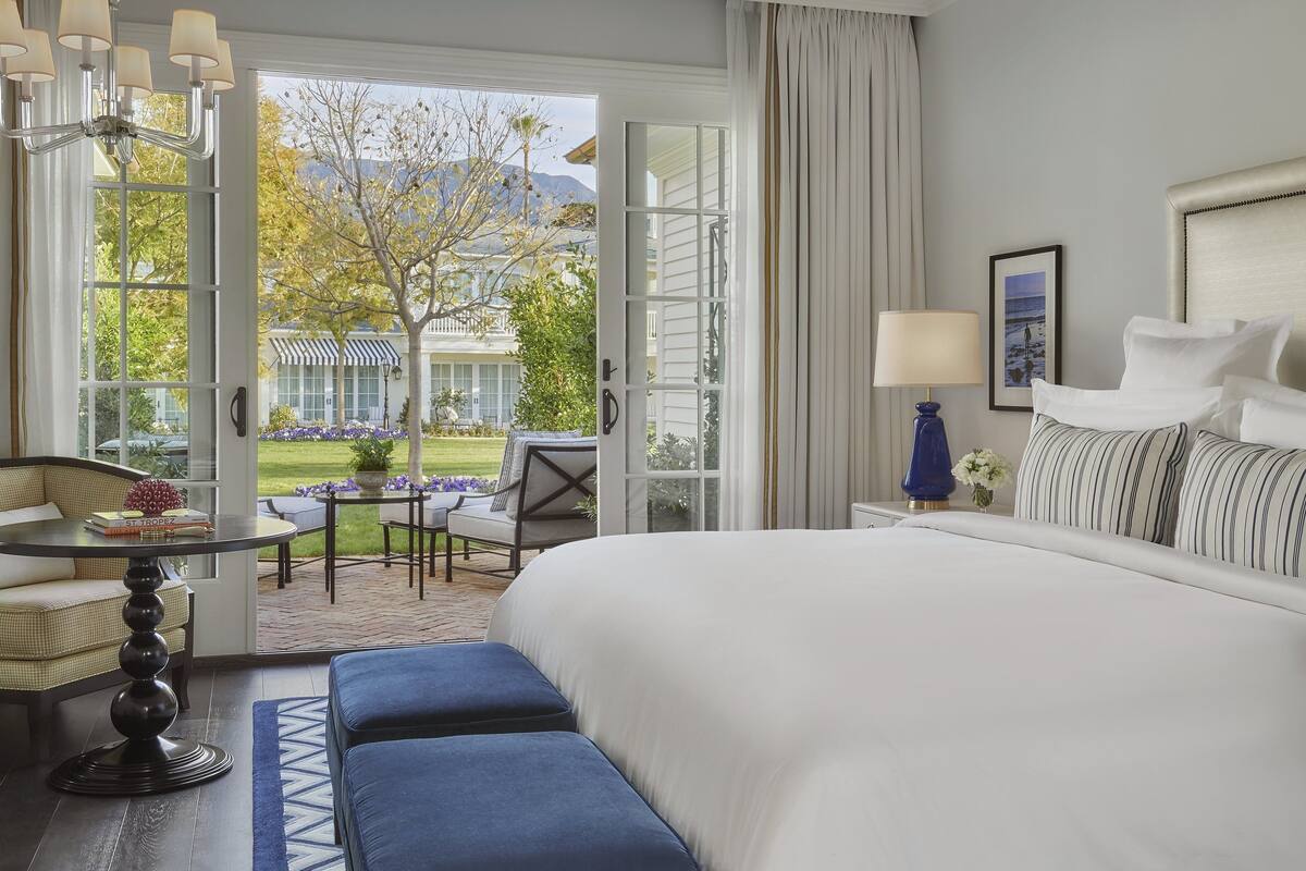 Hotelkamer met een groot bed, een zithoek met een tafel en stoelen, en uitzicht op een gebouw en bomen.