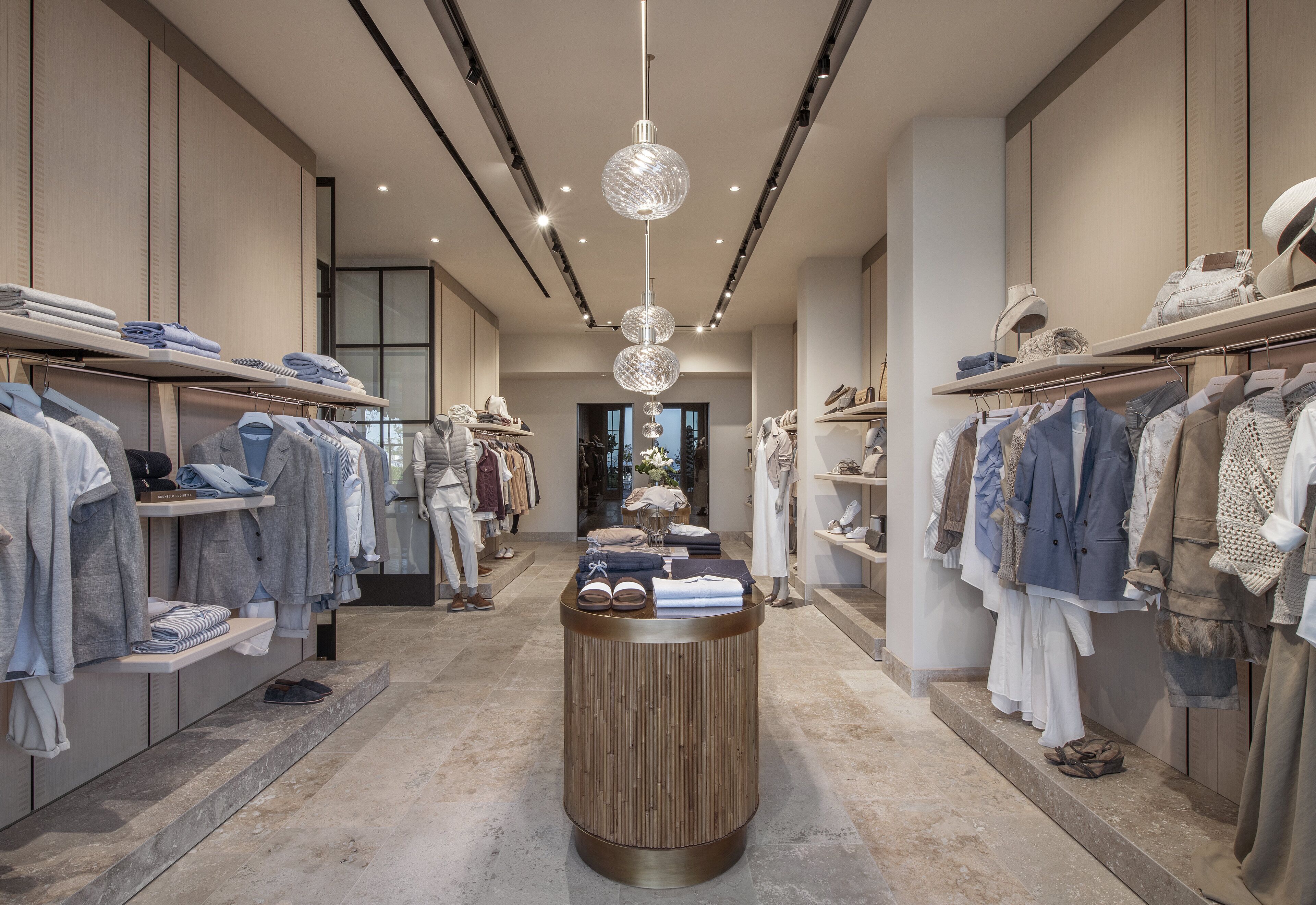 Une boutique moderne avec des présentoirs à vêtements bien organisés, une table centrale et un élégant luminaire suspendu.