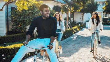 A paved pathway with bicycles, palm trees, and residential buildings in the background.