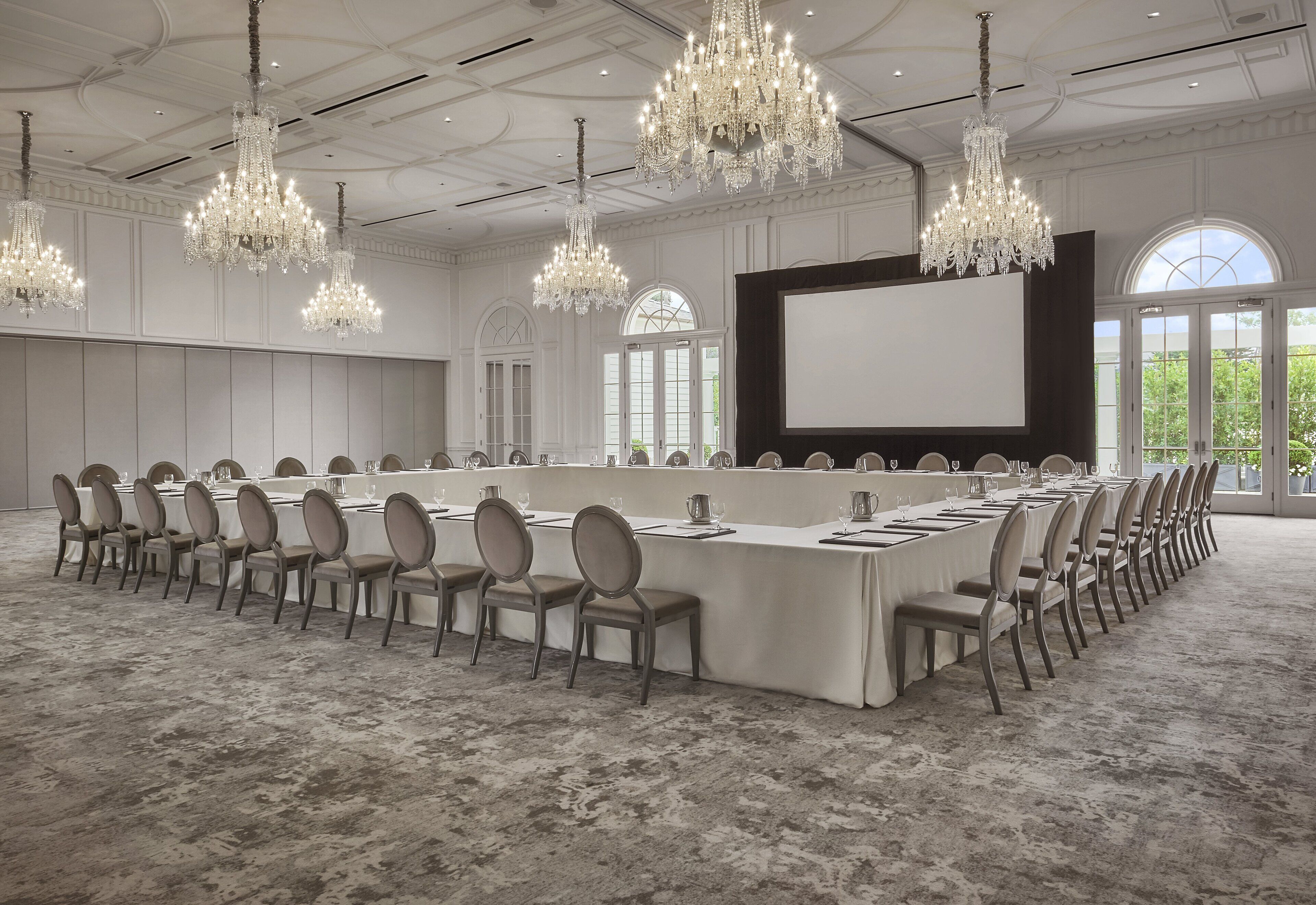 A conference room with a long table, chairs, a large screen, and chandeliers.