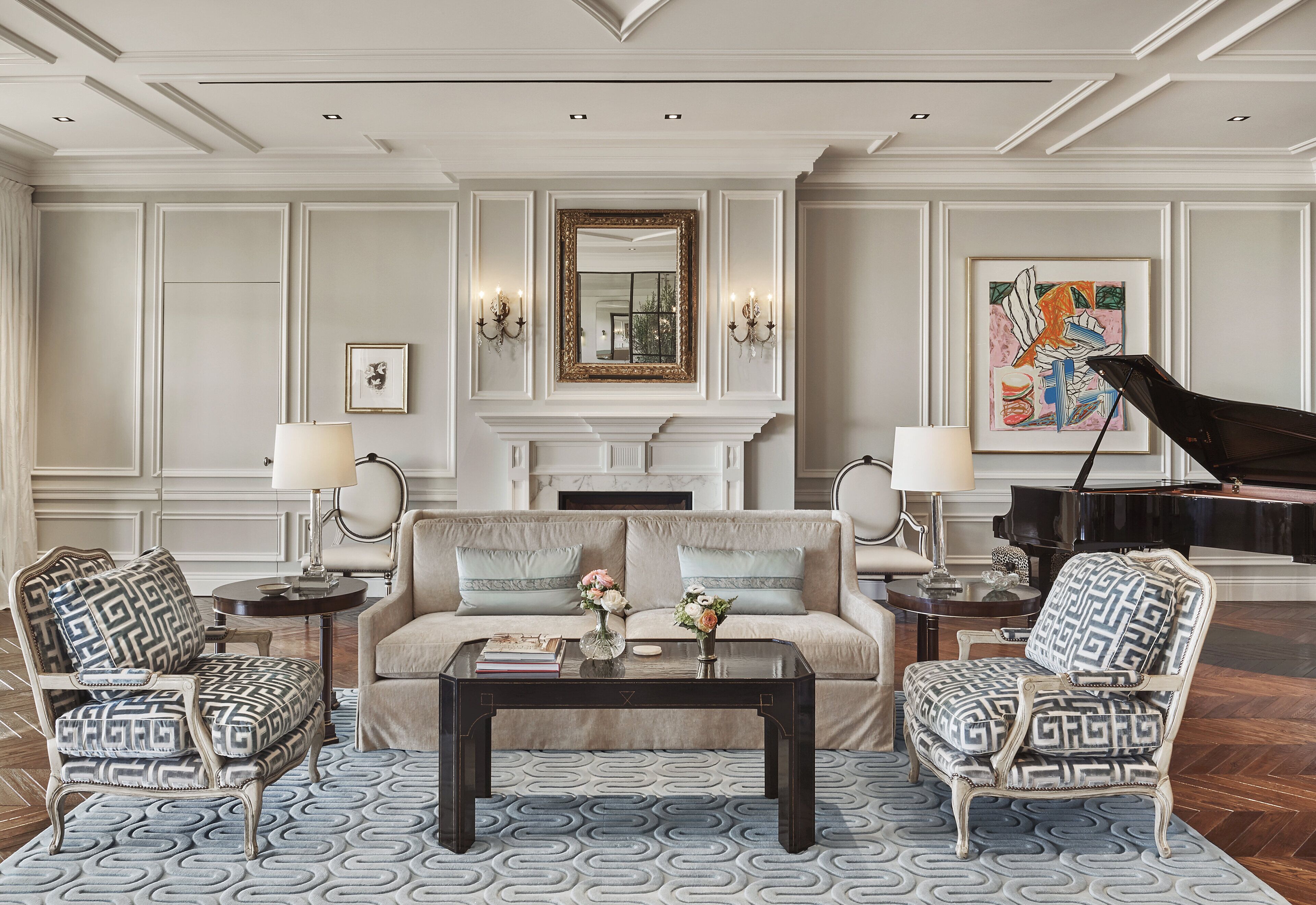 A formal living room with a sofa, two armchairs, a coffee table, a fireplace, and a grand piano.