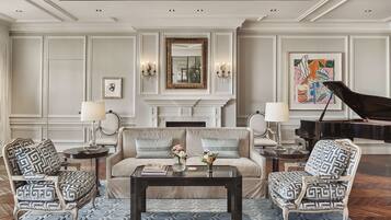 A formal living room with a sofa, two armchairs, a coffee table, a fireplace, and a grand piano.