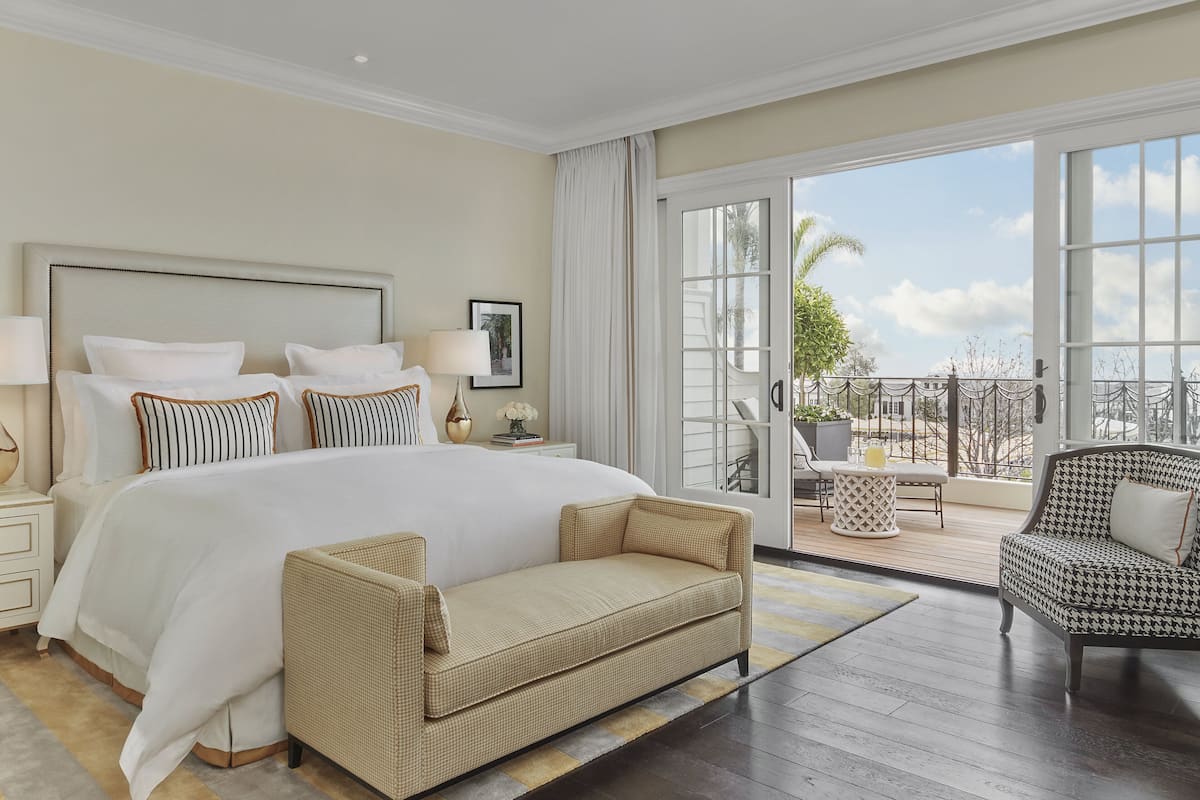 Een ruime slaapkamer met een groot bed, een bank, een gestreept fauteuil en een balkon met uitzicht.
