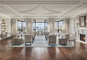 A spacious living room with a herringbone wood floor, large windows with curtains, a fireplace, and a view of the outdoors.