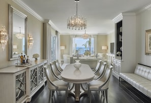 A dining area with a white table and chairs, a chandelier, and a view through a window.