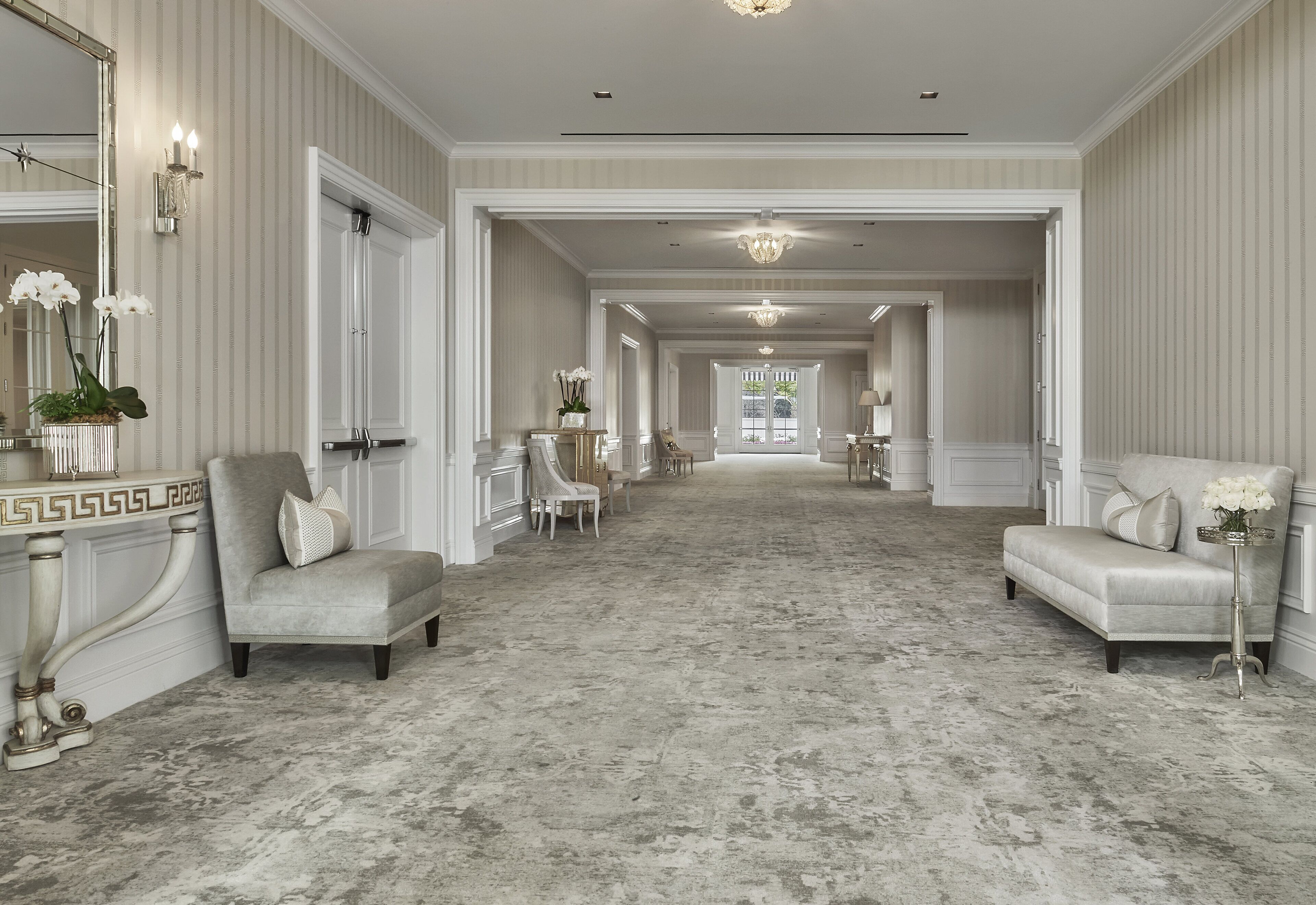 A spacious hallway with a marble floor, flanked by two armchairs and a table with a vase of flowers.